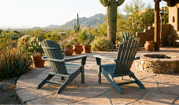 Two gray-blue Adirondack chairs on a desert patio with saguaro cacti, terracotta pots, a stone fire pit, and mountain views in the background